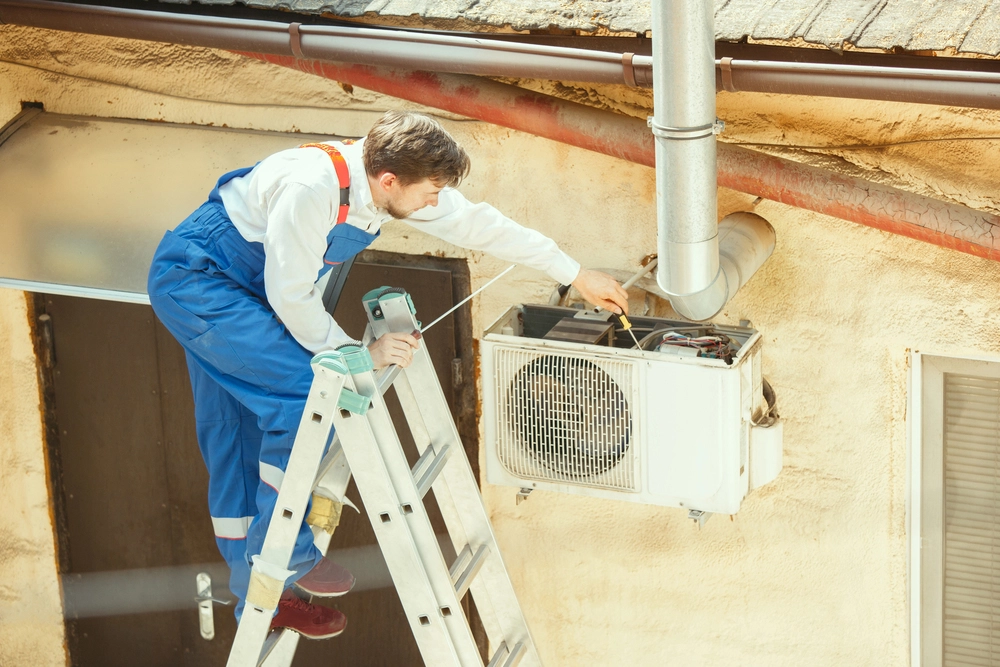 Home 2 An image of an HVAC technician on a ladder installing or repairing an outdoor air conditioning unit on a residential building.